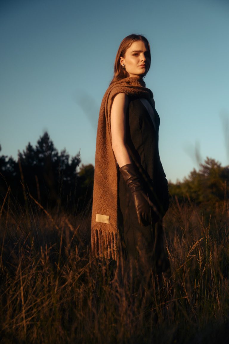 Model draagt een lange sjaal en staat in lang gras