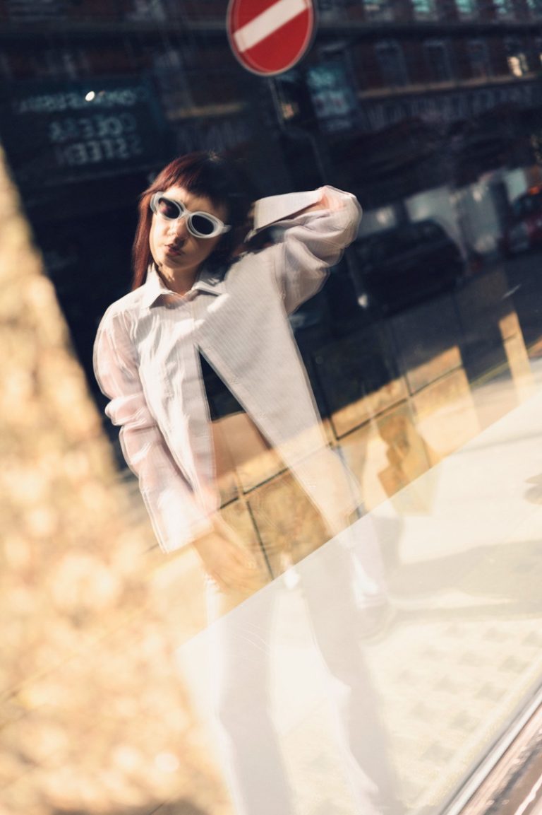 Edgy model staring at her window reflection in the streets of London dressed in Dior blouse